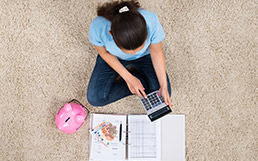 Žena sedí na koberci a s kalkulačkou počíta peniaze