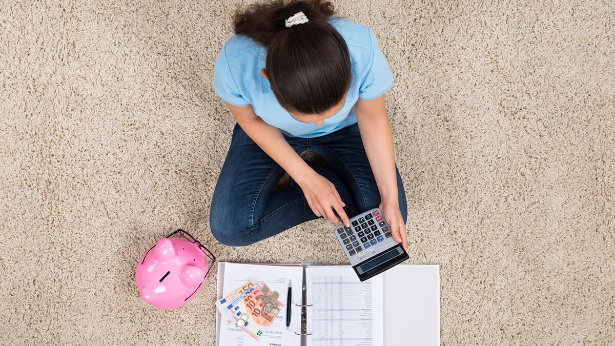Žena sedí na koberci a s kalkulačkou počíta peniaze